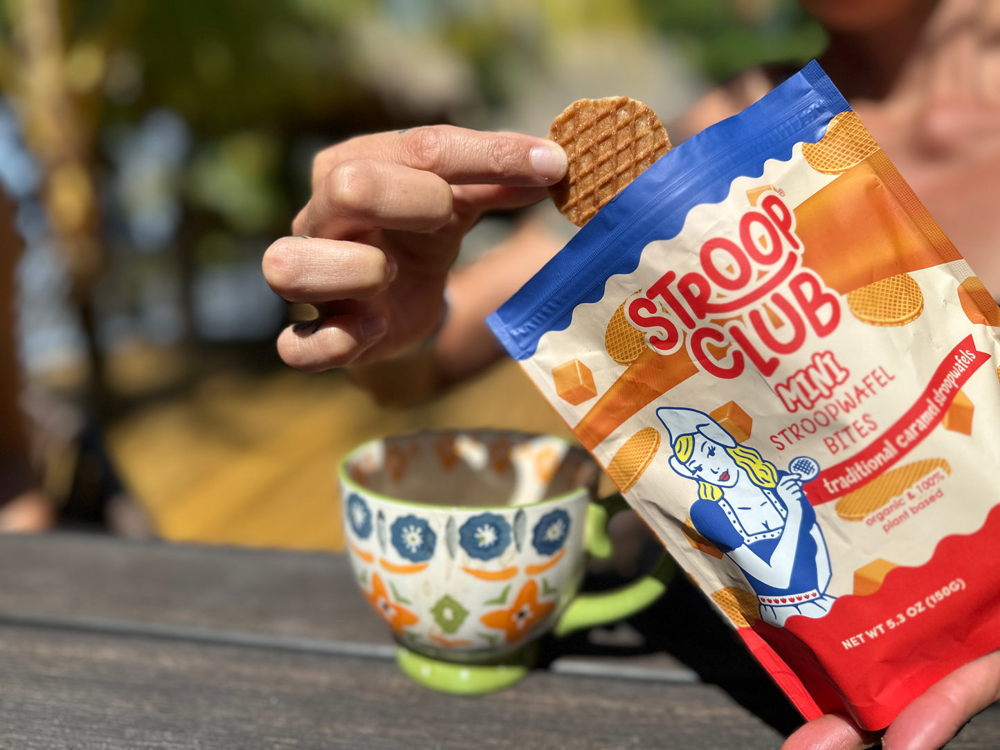 Photo of someone getting a mini stroopwafel out of the bag, next to a coffee cup.